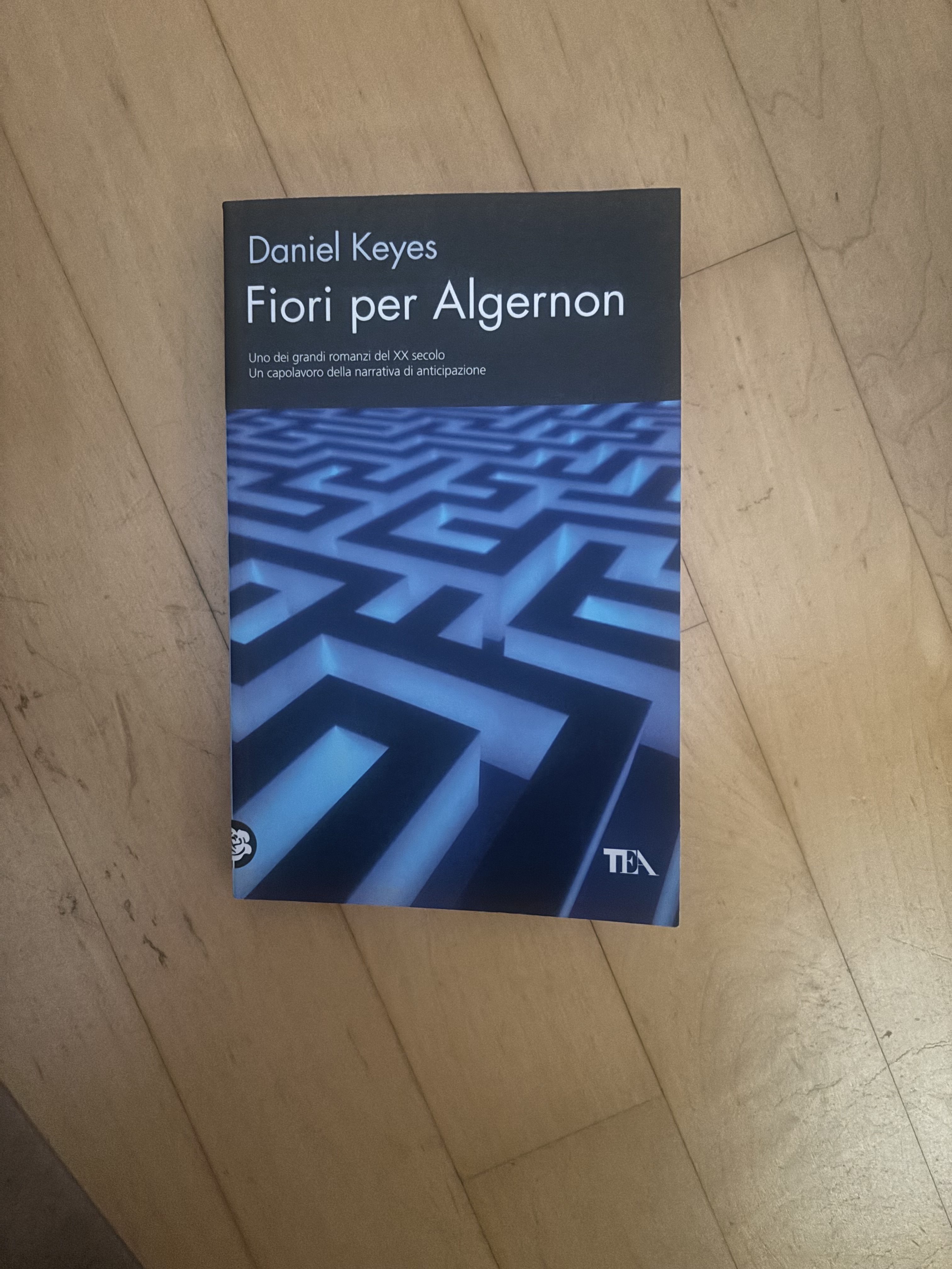 The book cover of 'Fiori per Algernon' by Daniel Keyes featuring a maze design on a blue background, displayed on a wooden surface.